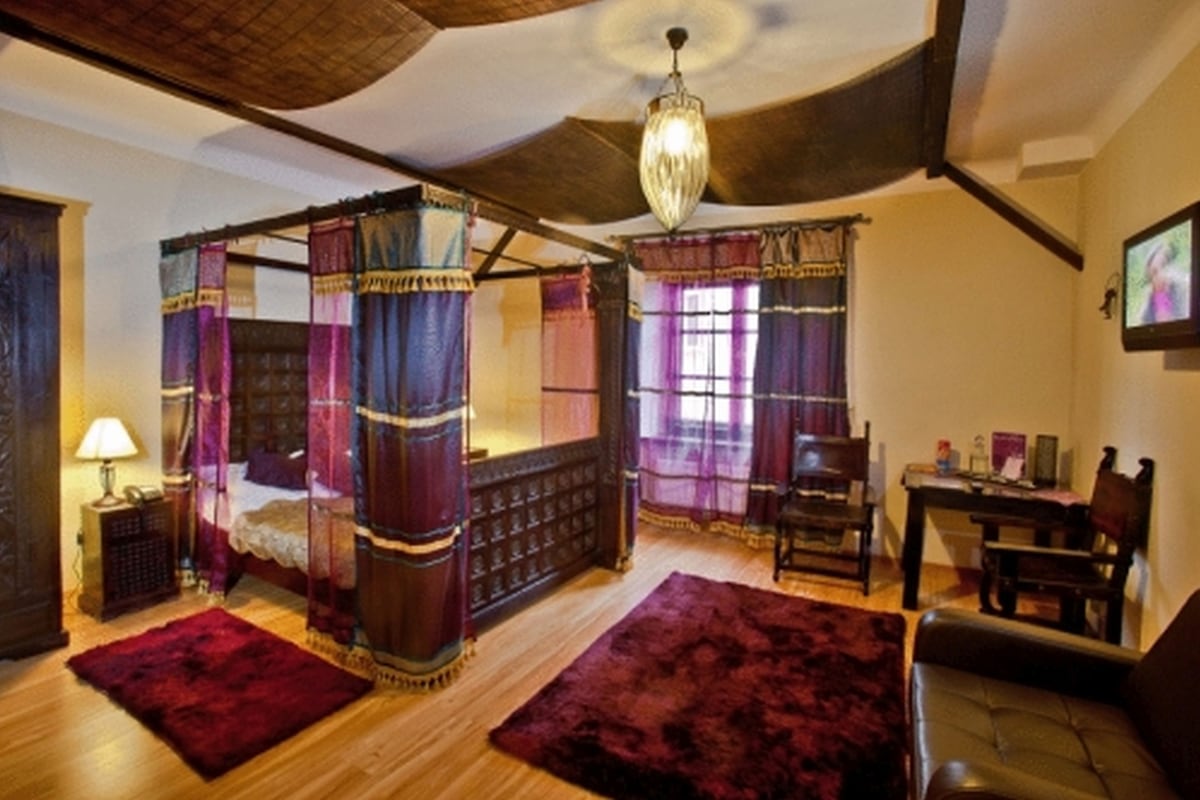A traditional four-poster bed with a canopy, a wooden floor, and a chandelier.