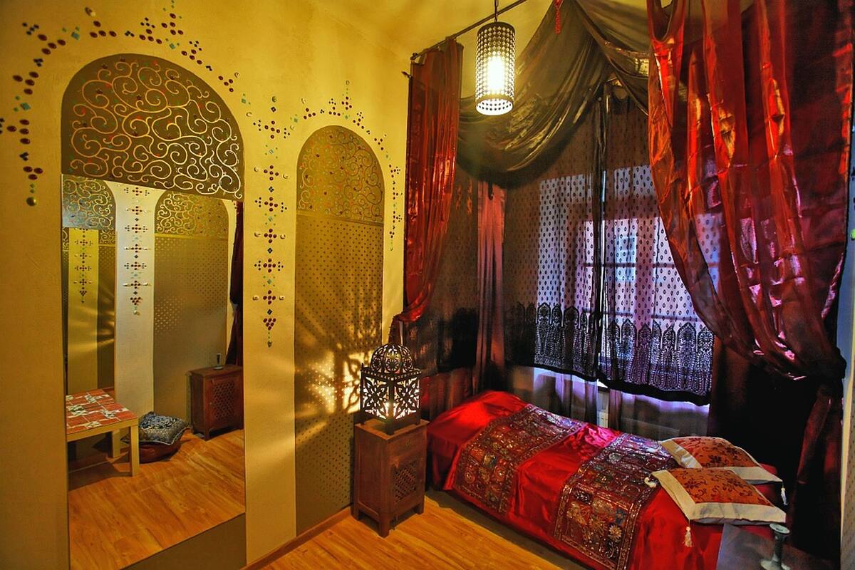 A room with a bed, a nightstand, a lamp, a mirror, and a window with curtains.