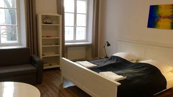 Un dormitorio con cama, mesita de noche, escritorio y ventana con cortinas.