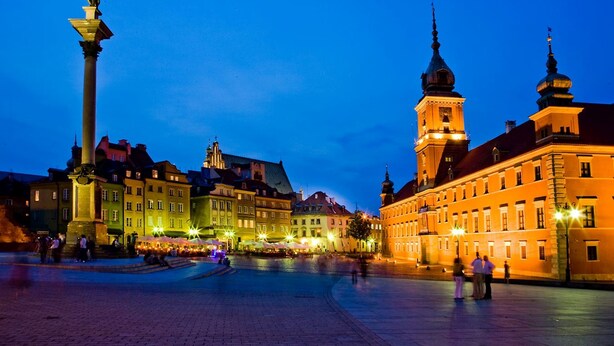 A historic square with a prominent statue, traditional buildings, and a tower. - Castle Inn (Warsaw)