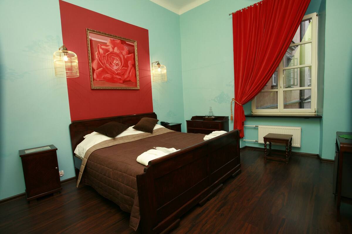 A bedroom with a large bed, a red curtain, a framed picture, and a window.