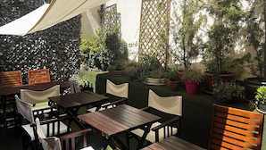 An outdoor patio with wooden tables and chairs, surrounded by potted plants and a decorative wall. - Castle Inn (Warsaw)
