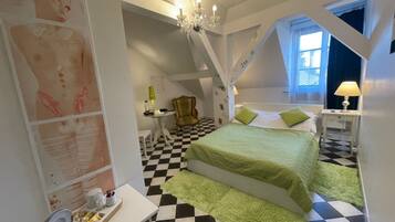 A bedroom with a checkered floor, a bed with green bedding, a chandelier, and a small table with a lamp.