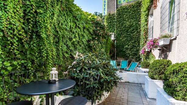 A courtyard with a table and chairs, surrounded by lush greenery and a white wall. - The Secret Garden Hostel (Kraków)