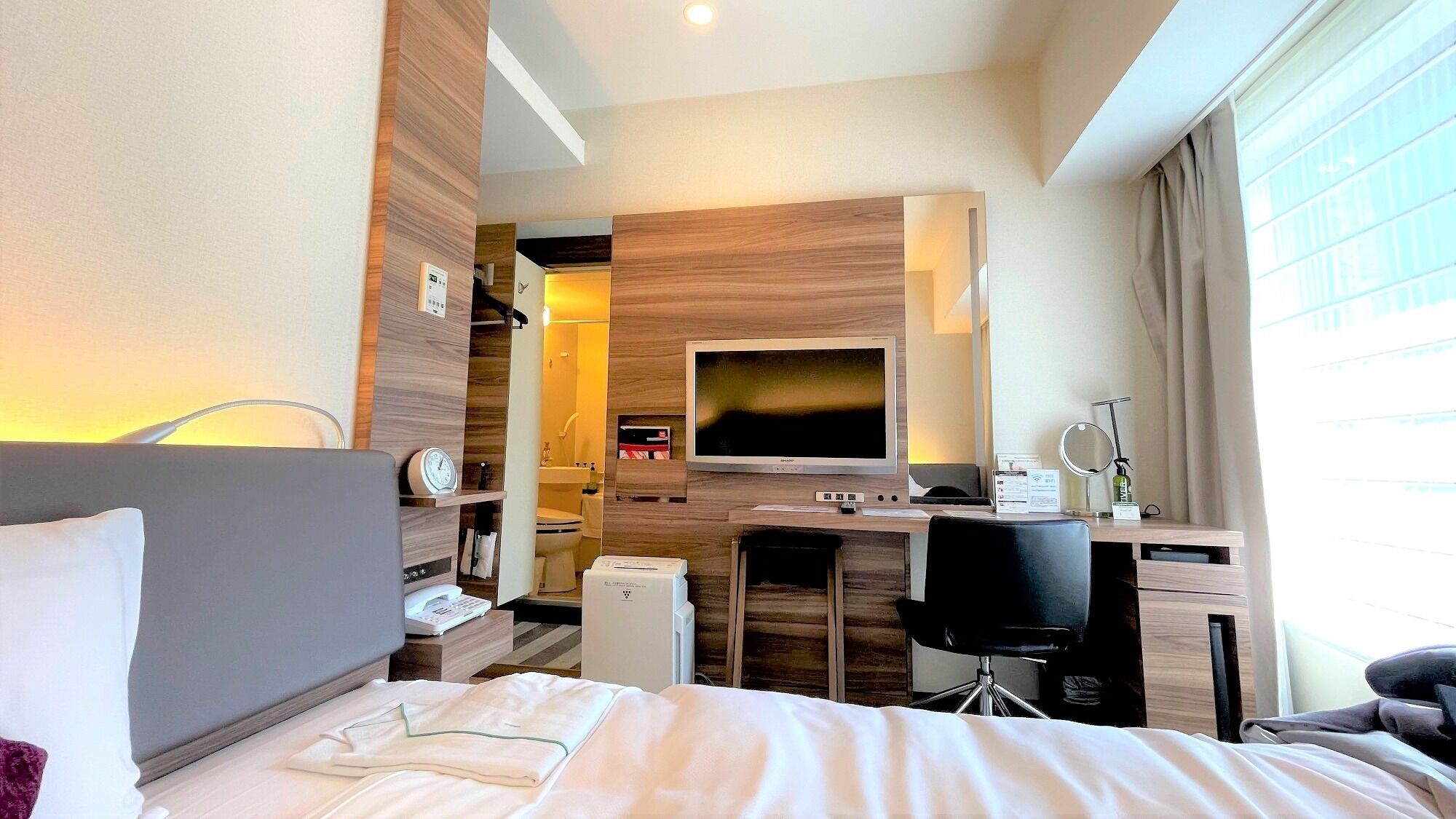 A hotel room with a bed, desk, chair, TV, and a bathroom visible through an open door.