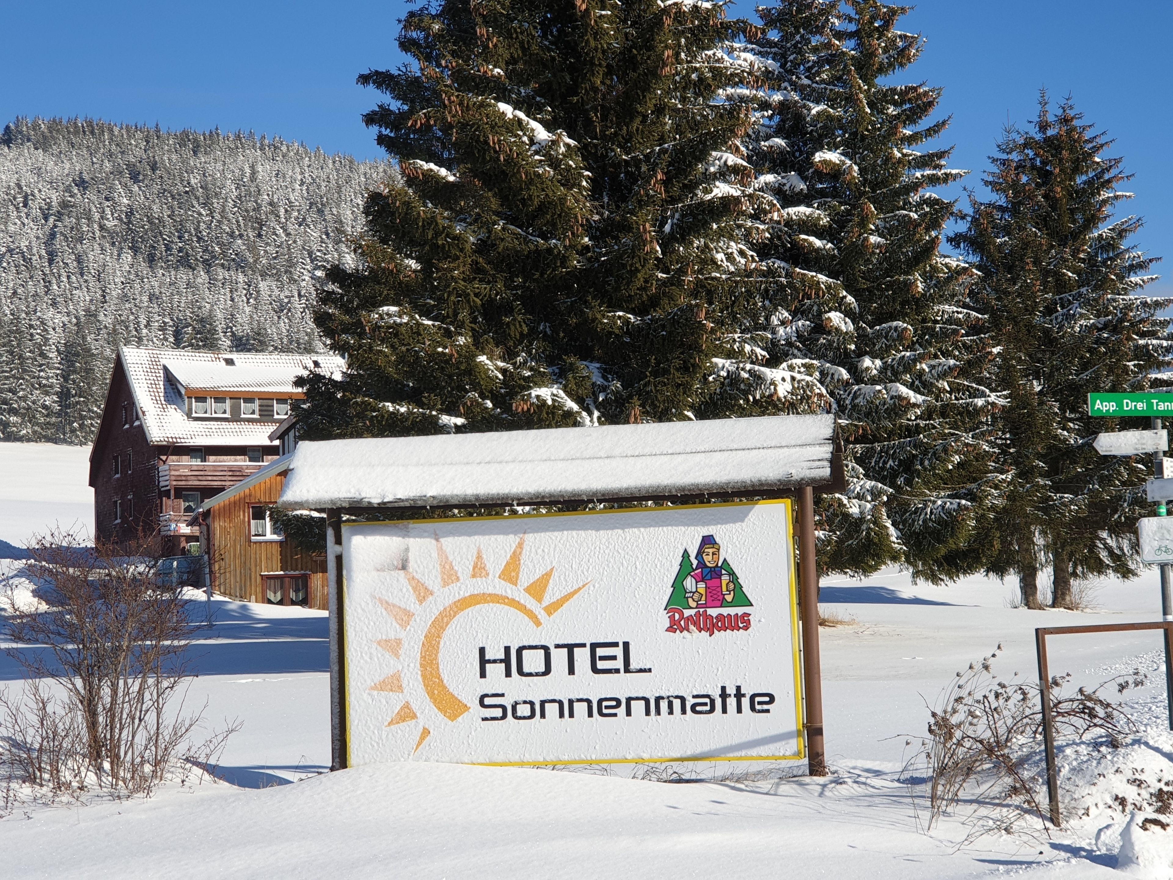 Señal de HOTEL Sonnenmatte con un símbolo de sol y un paisaje de montaña al fondo.