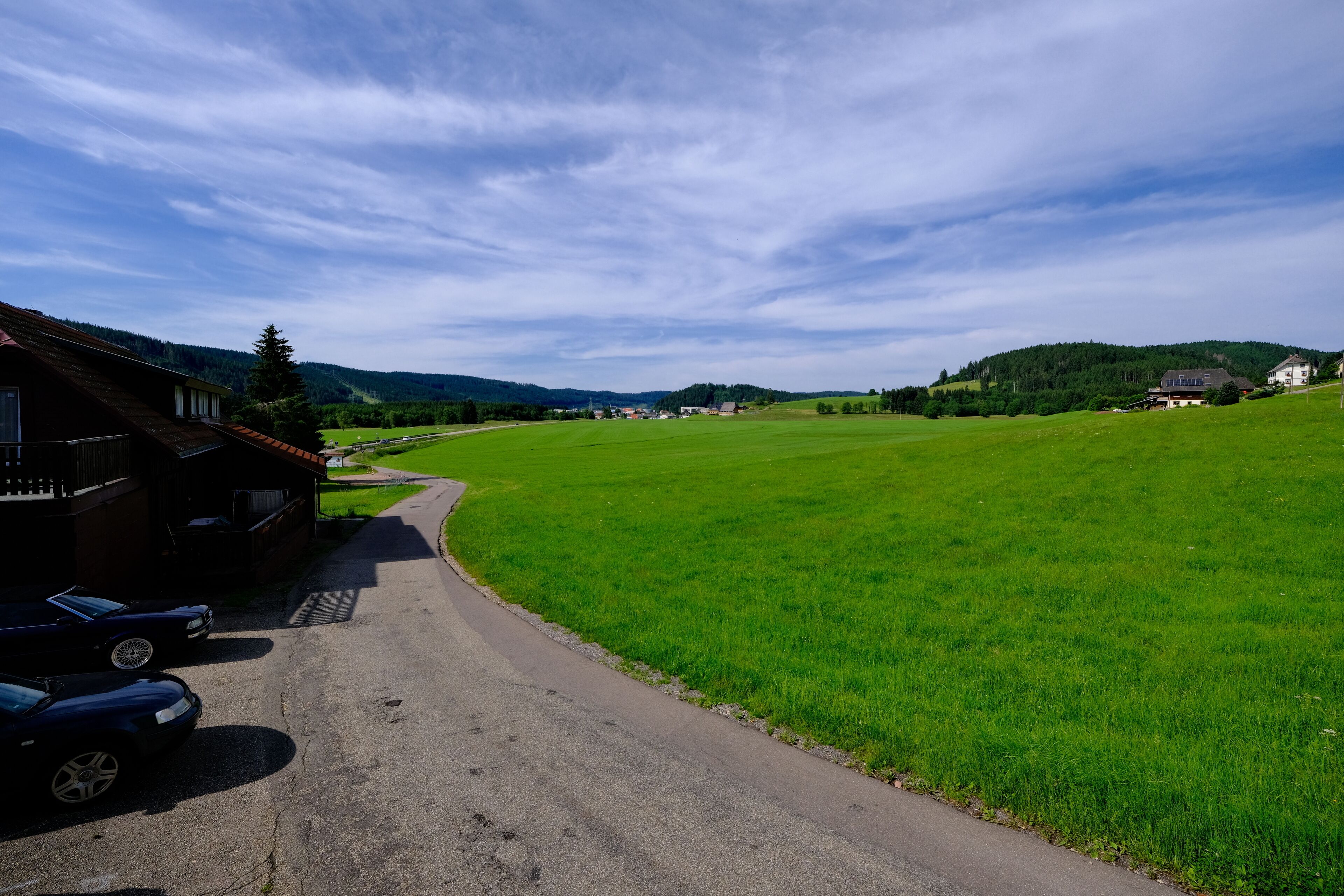 Una strada di campagna che porta a una casa con un'auto nei pressi.