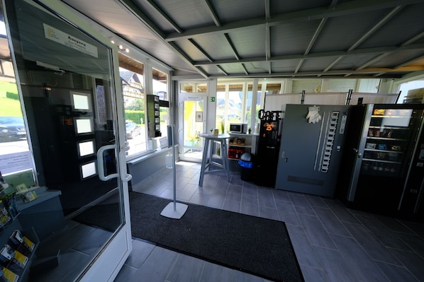 Interior de una cafetería moderna con un quiosco de autoservicio, una máquina de café y un refrigerador.