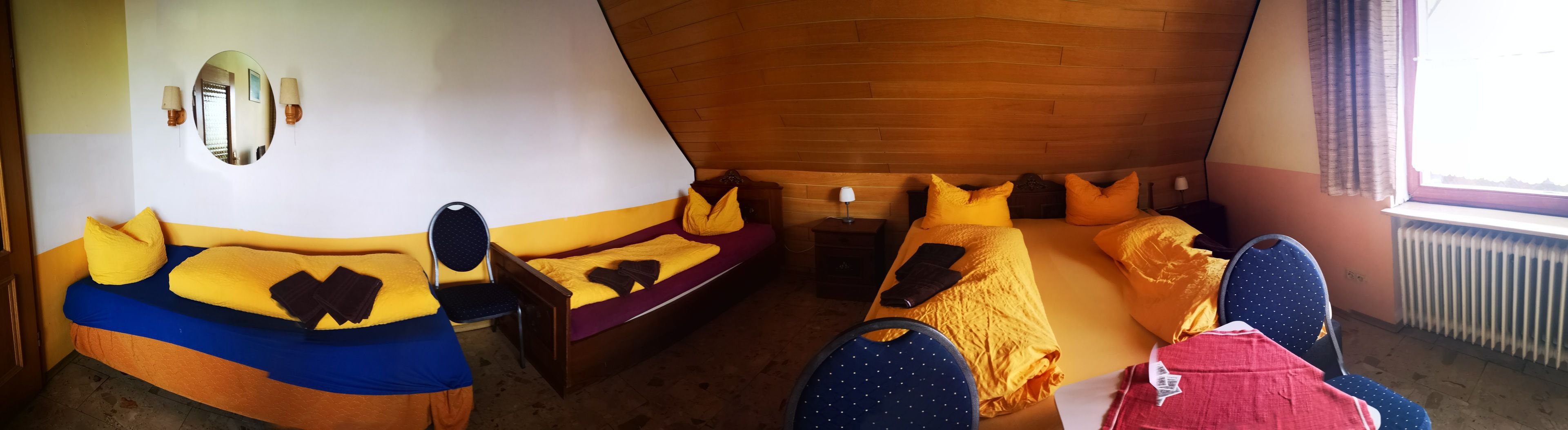 Une chambre avec deux lits, chacun agrémenté de draps jaunes et bleus, un plafond en bois et une fenêtre avec des rideaux.