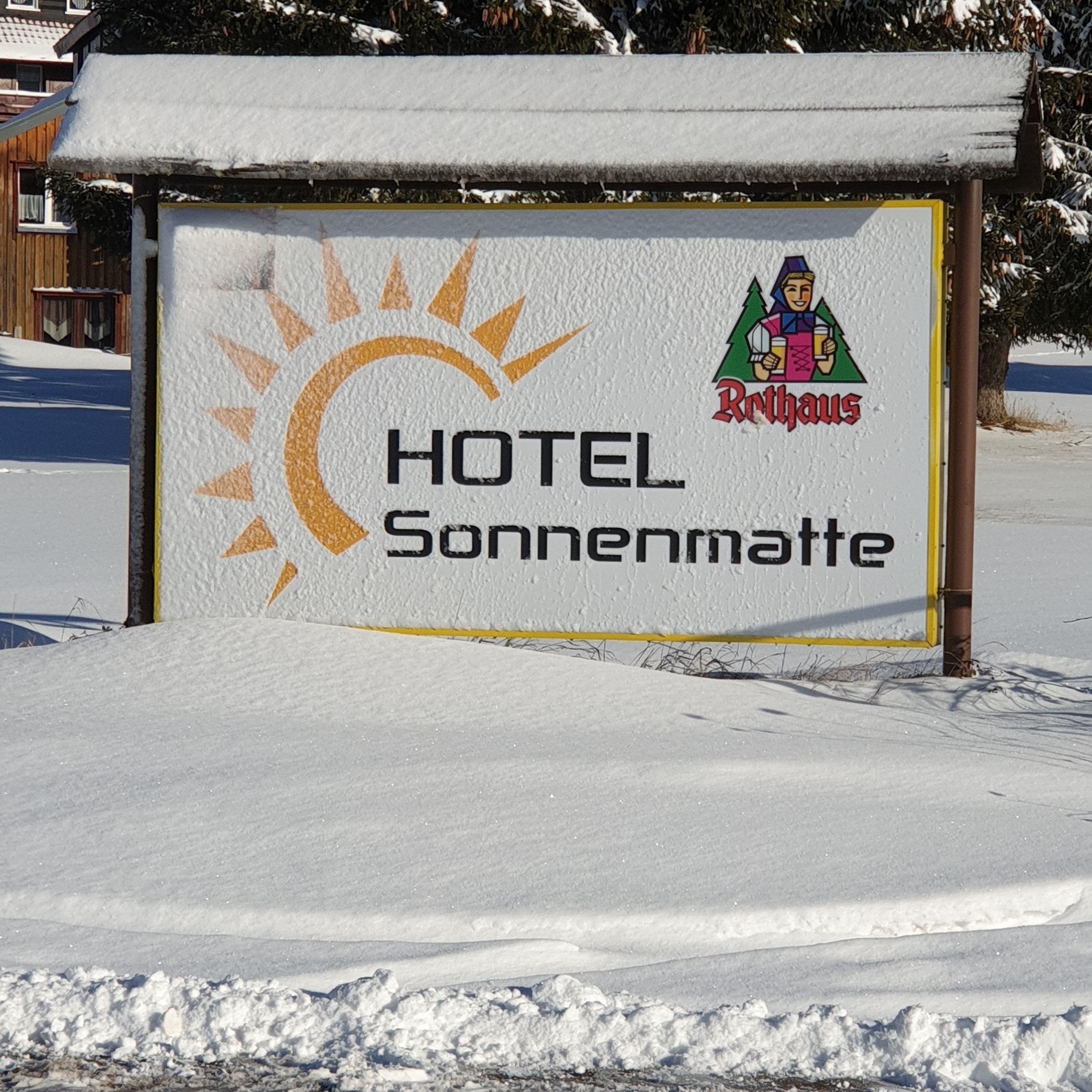 A sign for Hotel Sonnenmatte with a sun and mountain graphic.