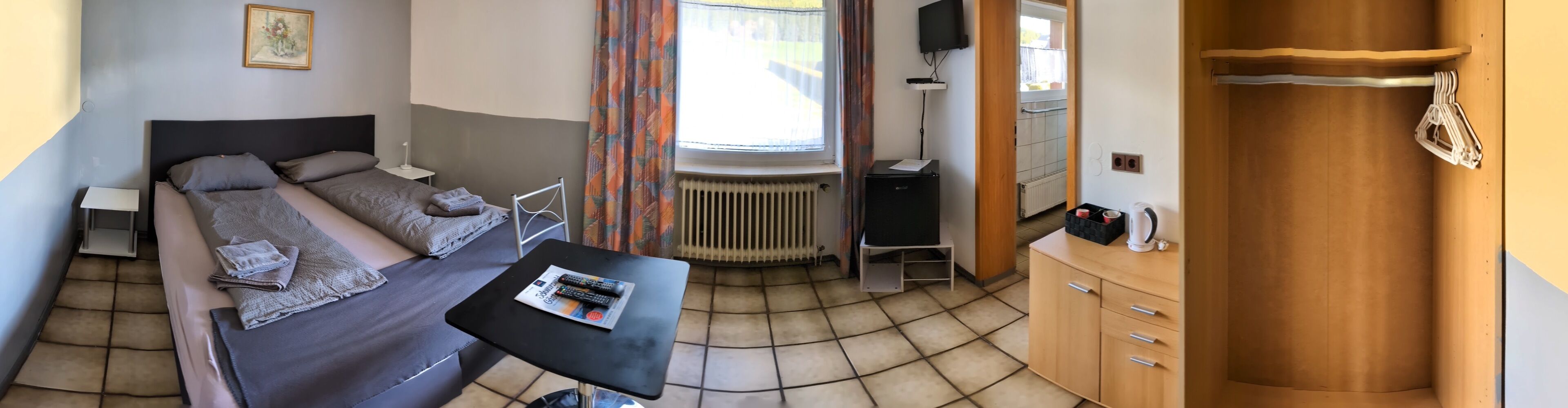 Una habitación con una cama, una mesita con mandos a distancia, un radiador y un armario de madera.