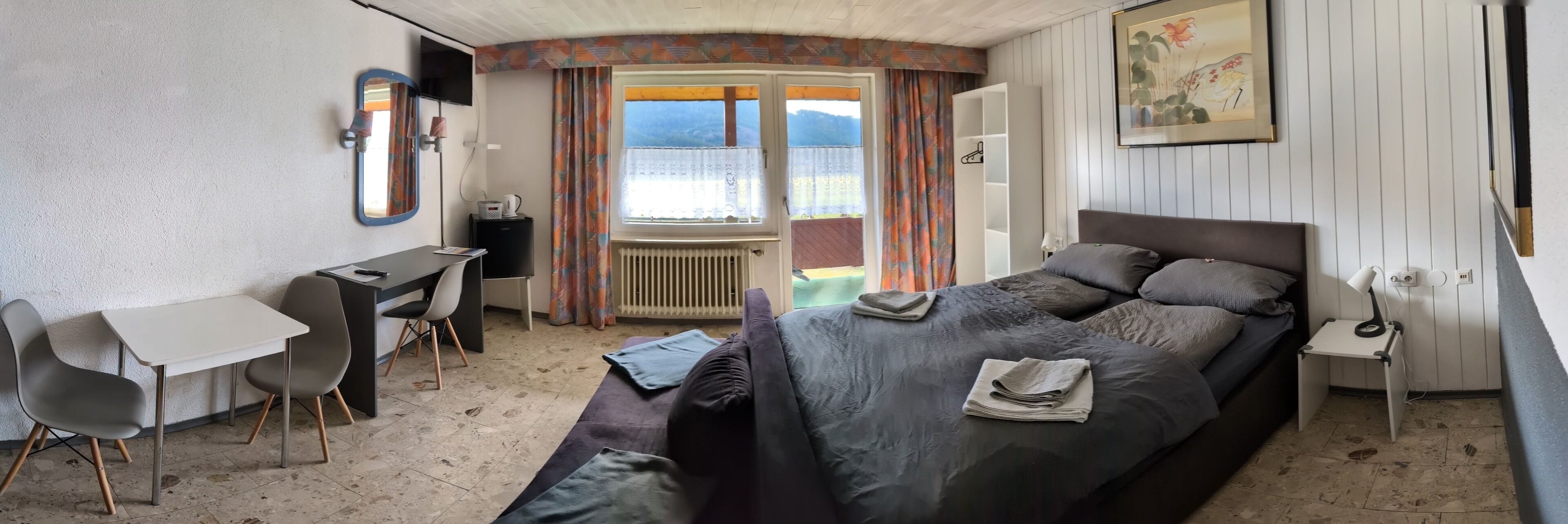 A bedroom with a bed, bedside table, lamp, and a desk with chairs.