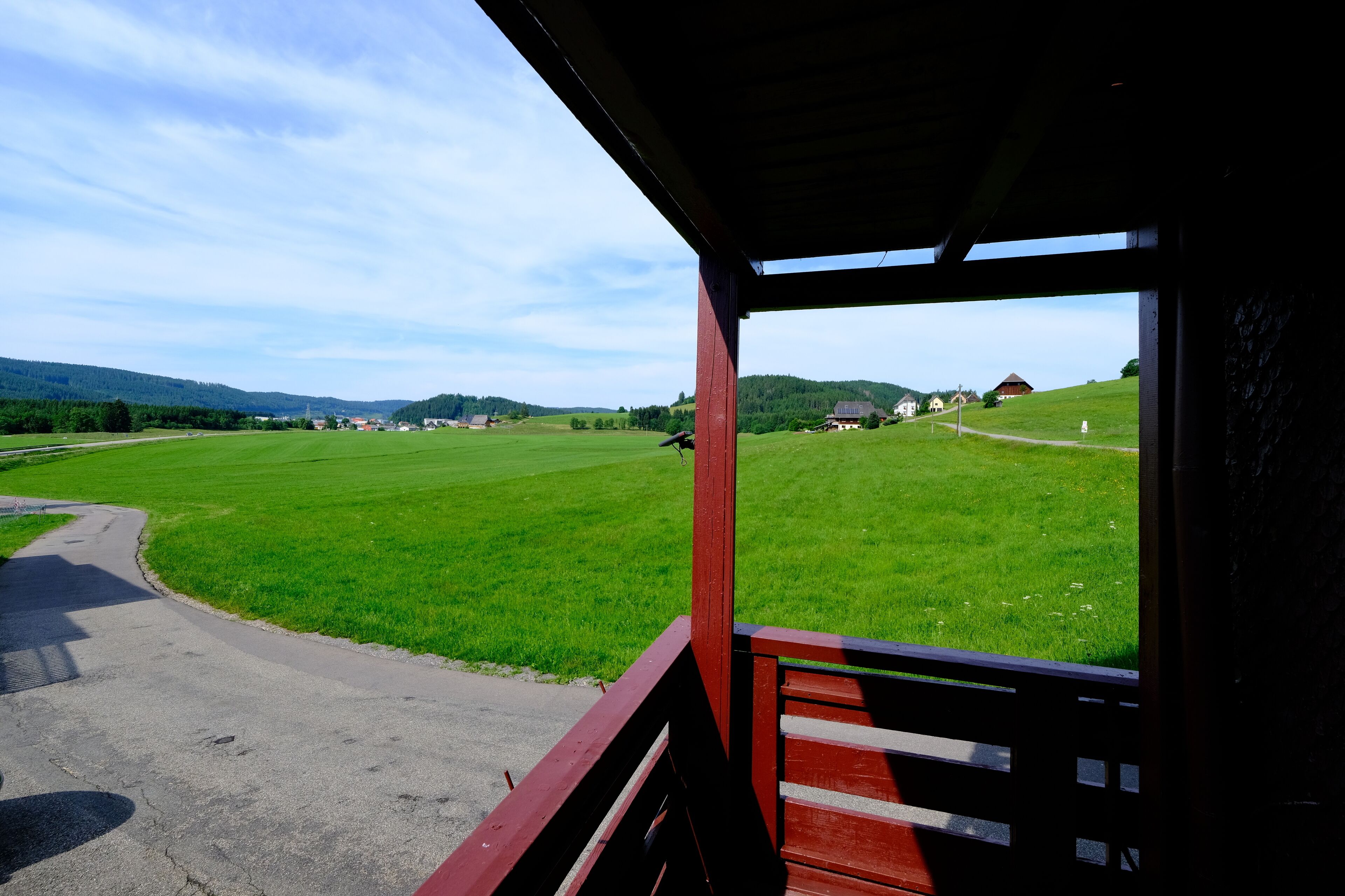 A view from a covered porch overlooking a green field with a road curving through it.