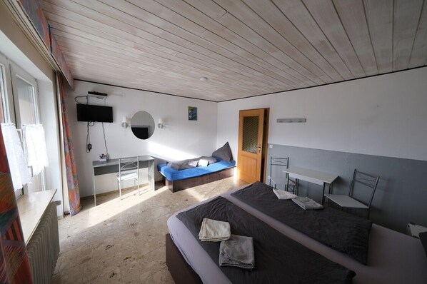 Un dormitorio moderno con una cama grande, un escritorio, un sofá azul y un televisor montado en la pared.