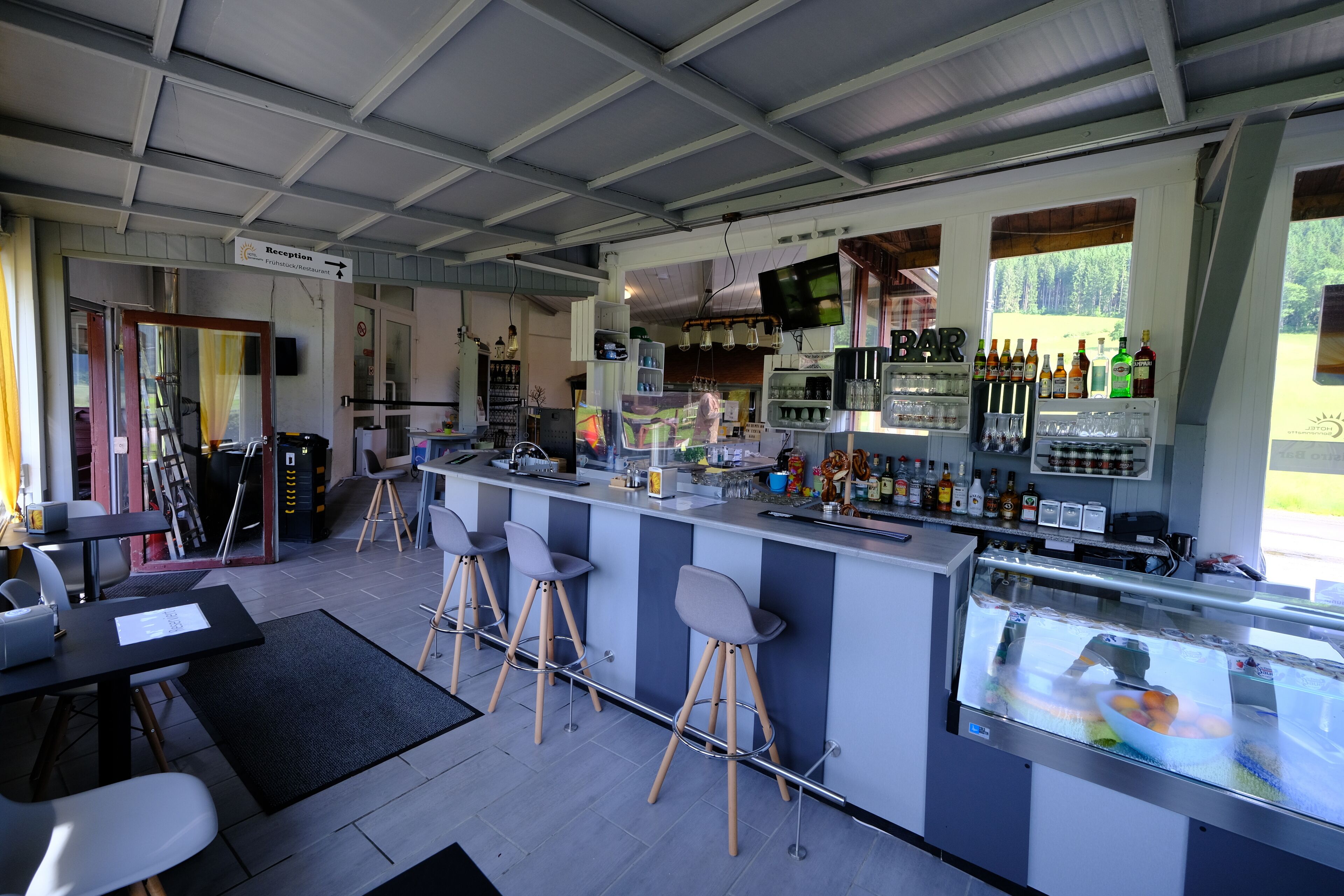 A bar area with stools, a reception desk, and a refrigerator stocked with beverages.