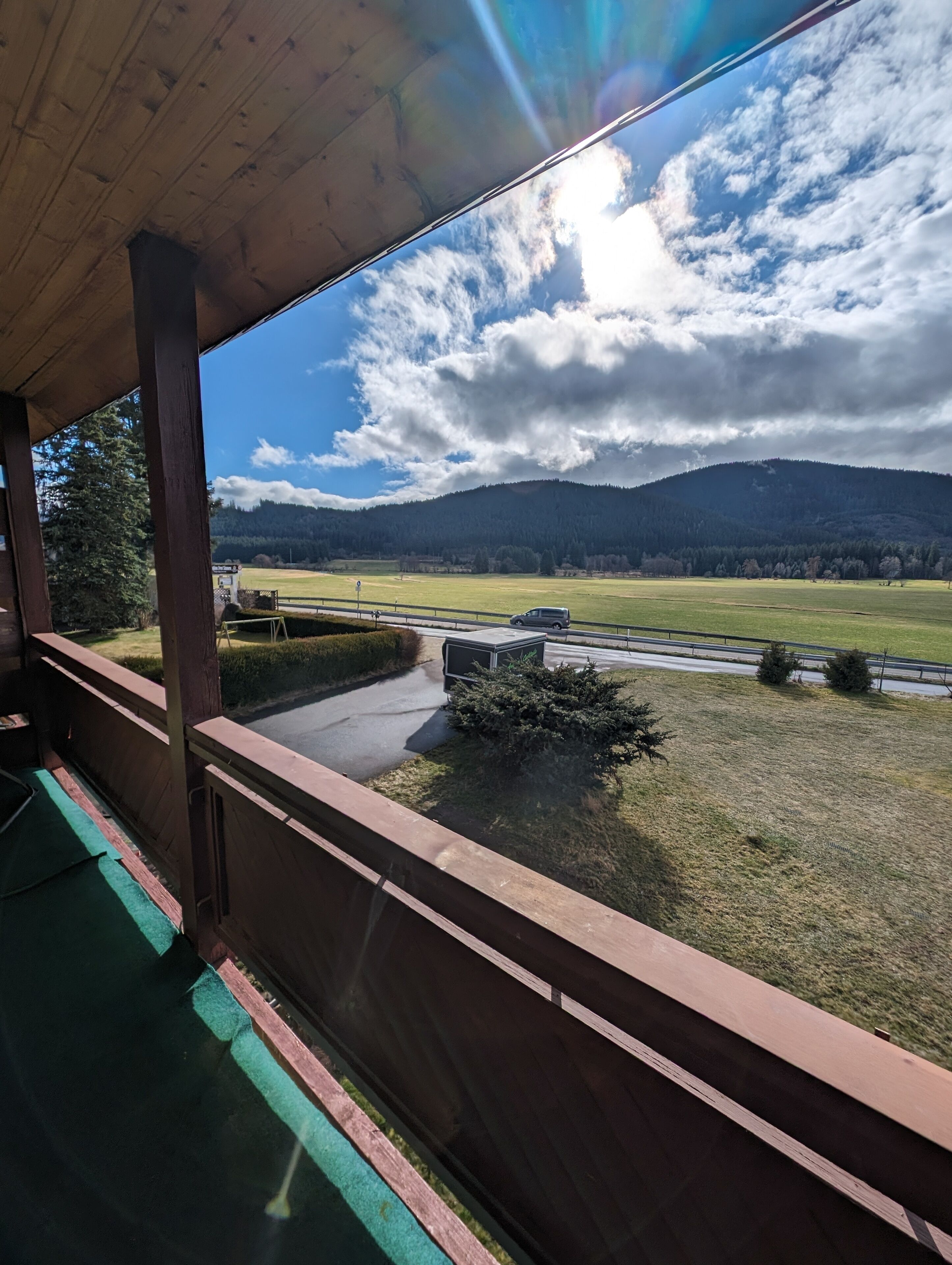 A balcony with a view of a road, a grassy field, and a mountain in the distance.