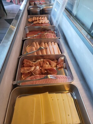 Buffet com diversos alimentos, incluindo massas, carnes e queijos.