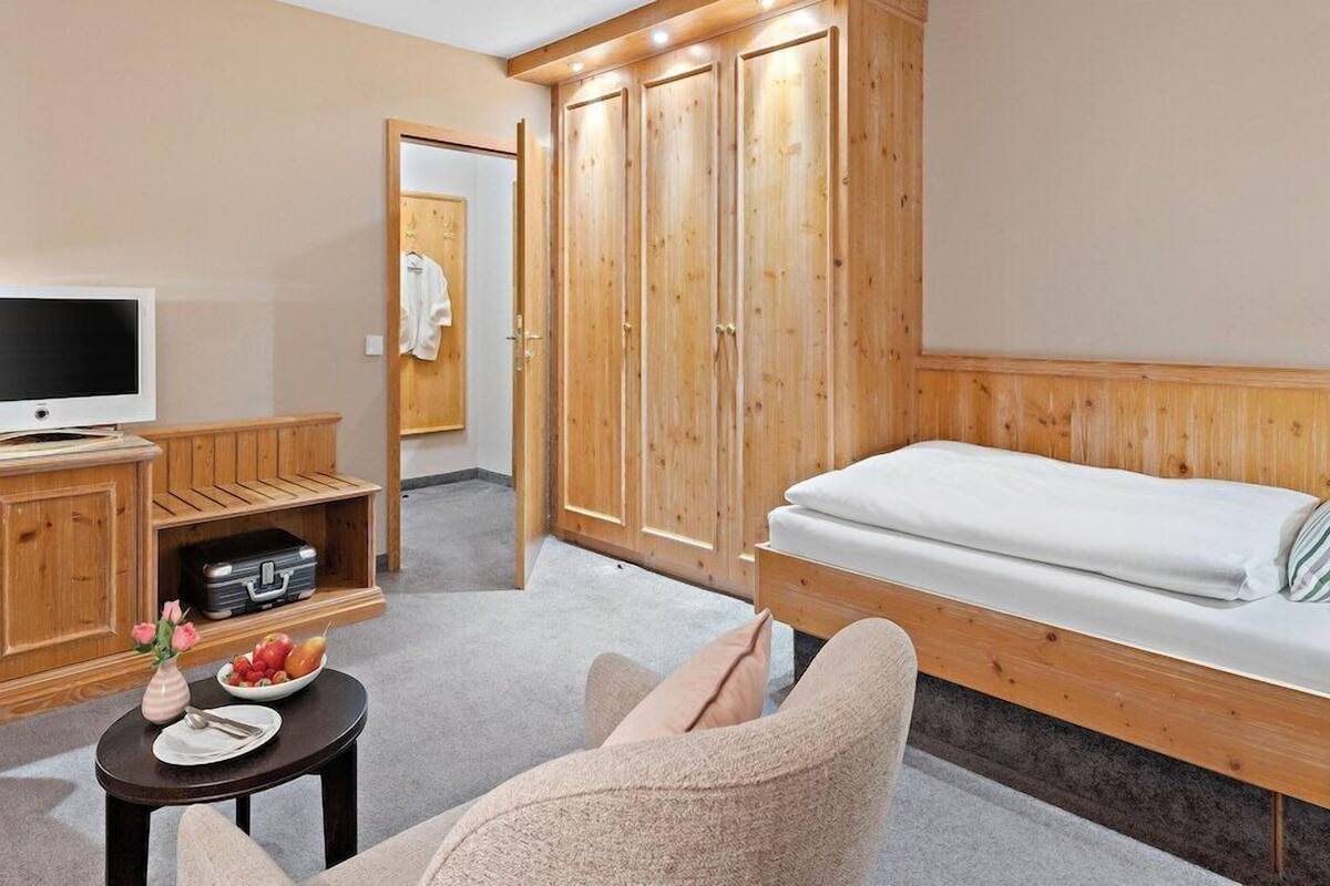 A room with a bed, a TV, a wardrobe, a small table with a vase and fruit, and a chair.