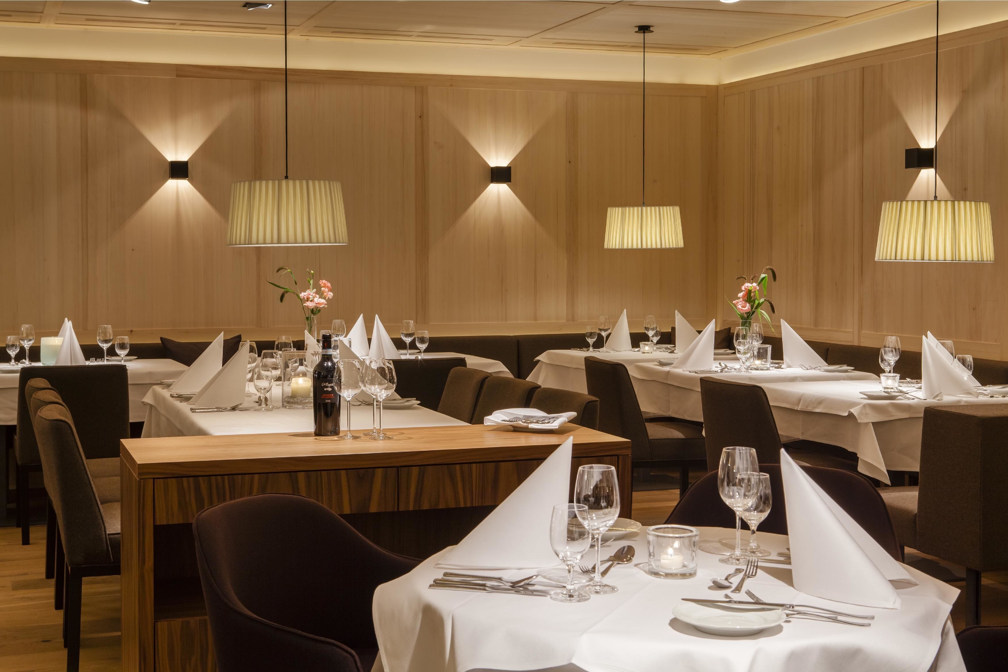 Ein Restaurant mit mehreren für den Essensgenuss gedeckten Tischen, jeweils mit weißen Tischdecken und ordentlich drapiertem Besteck.