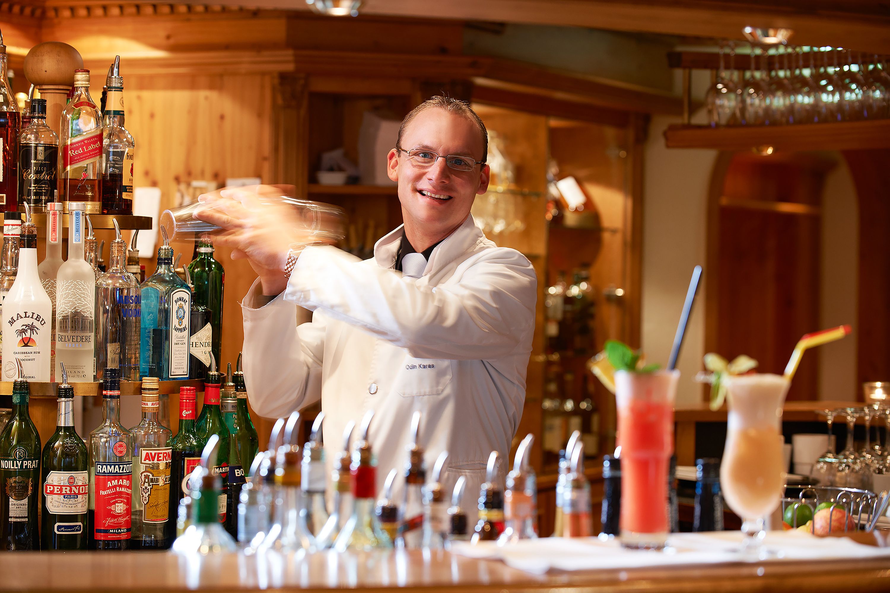 Zona de bar con varias botellas de alcohol y dos bebidas sobre la barra.