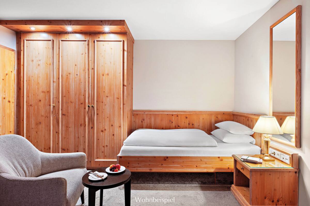 A hotel room with a bed, a chair, a small table with a plate of fruit, and wooden wardrobes.