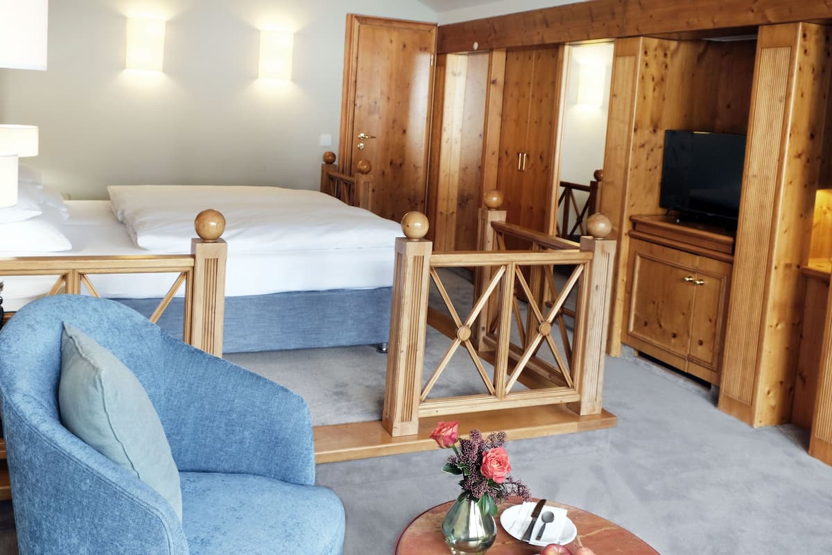 A hotel room with a bed, a blue armchair, a small table with a vase of flowers, and wooden furniture.