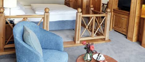 A hotel room with a bed, a blue armchair, a small table with a vase of flowers, and wooden furniture.