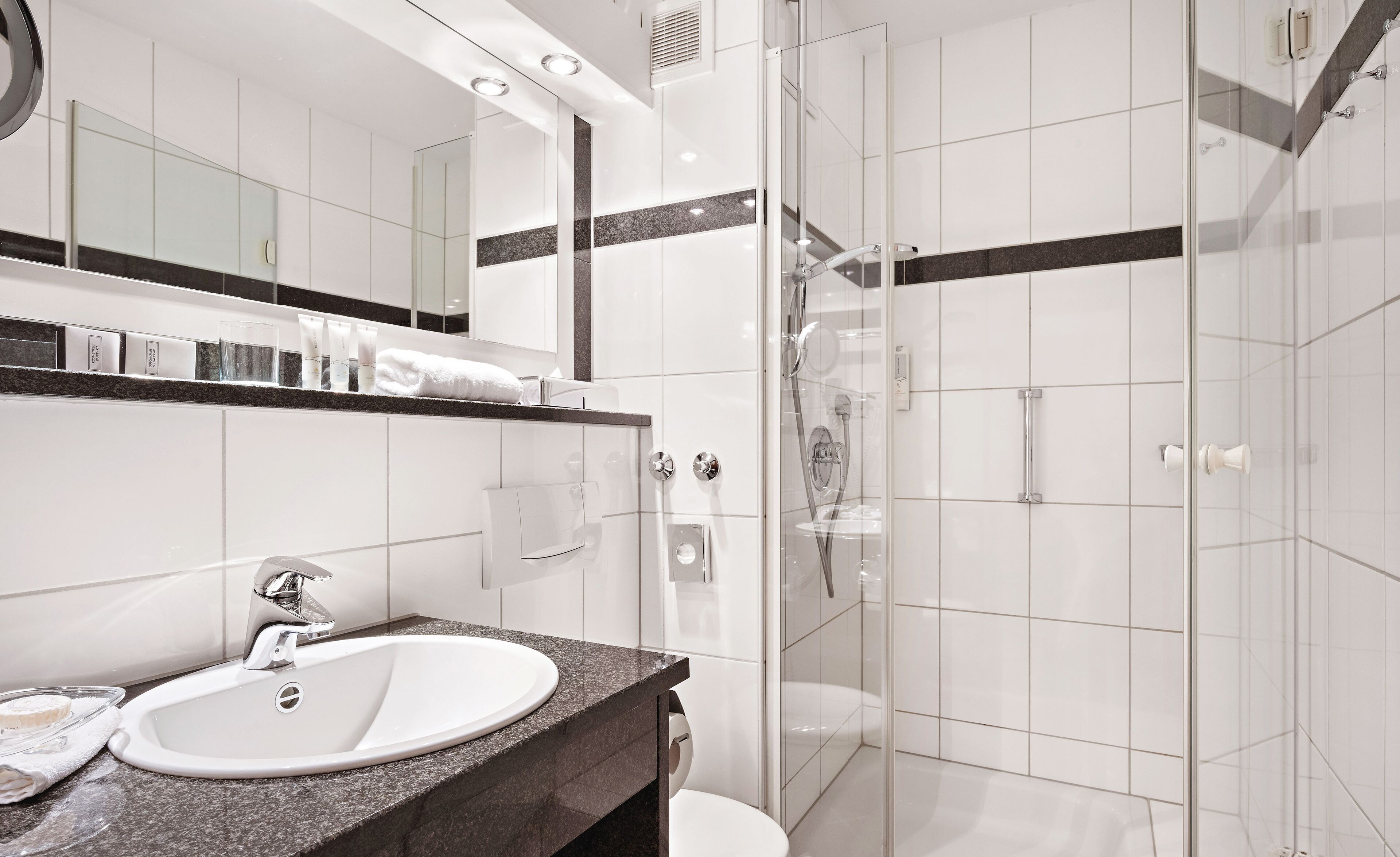 A modern bathroom with a granite countertop sink, a glass shower enclosure, and a large mirror above the sink.