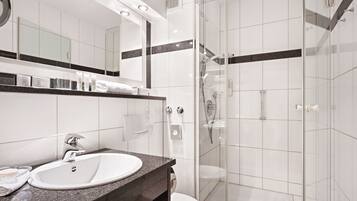 A modern bathroom with a granite countertop sink, a glass shower enclosure, and a large mirror above the sink.