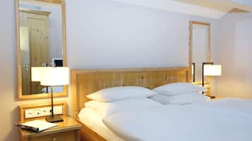 A hotel room with a wooden headboard, two bedside lamps, a nightstand with a lamp and a notepad, and a large mirror on the wall.