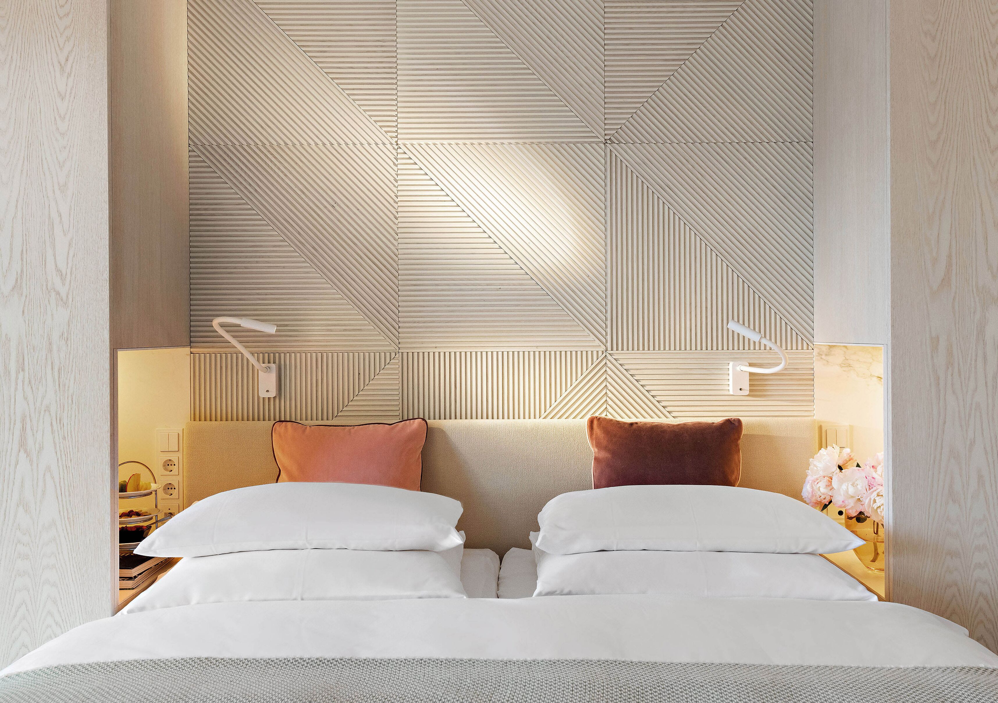 Une chambre d’hôtel avec un plafond orné de motifs géométriques, un lit avec une literie blanche et une table de chevet avec une lampe.