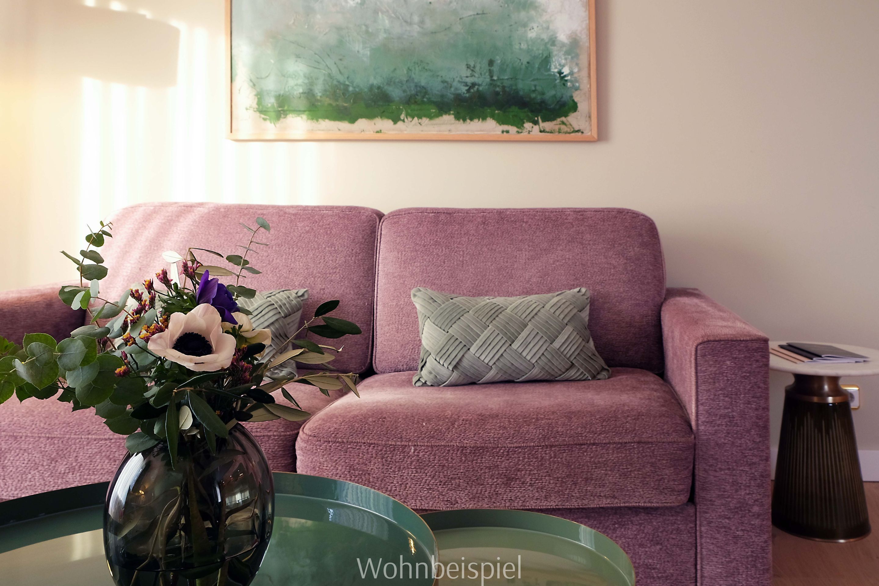 A living room with a pink sofa, a glass coffee table, and a vase with flowers.