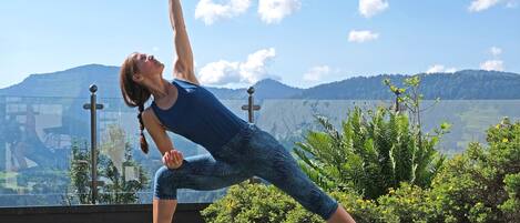Una persona realizando una postura de yoga sobre una colchoneta al aire libre, con montañas al fondo.