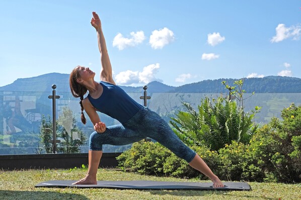 Una persona realizando una postura de yoga sobre una colchoneta al aire libre, con montañas al fondo.
