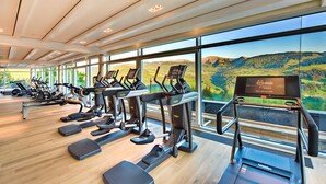 Un gimnasio con cintas de correr, elípticas y una pantalla de televisión, que cuenta con grandes ventanales con vistas a la montaña.