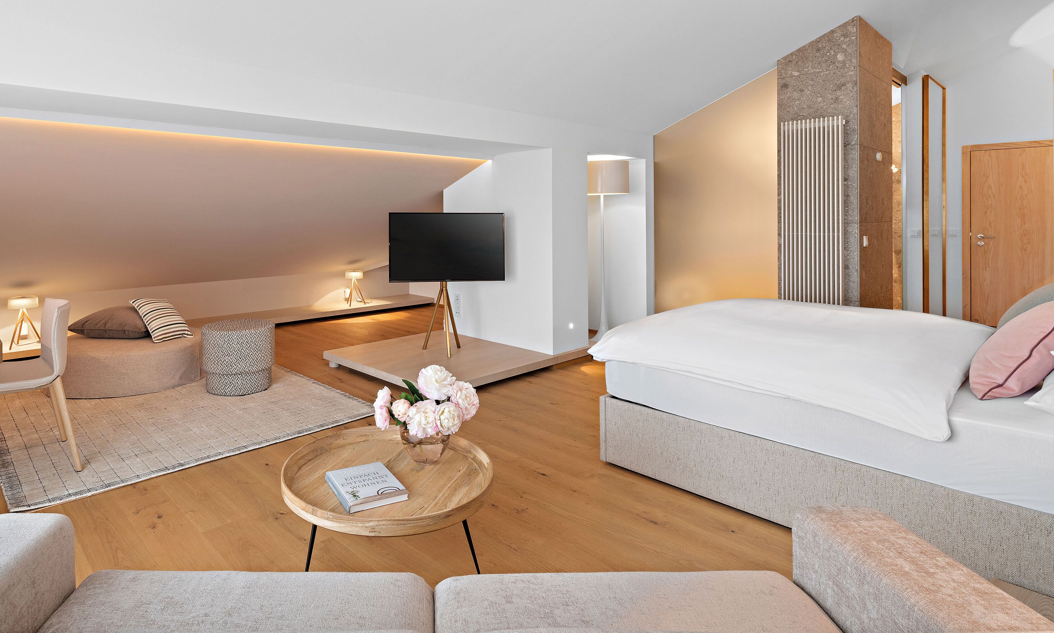 Een moderne slaapkamer met een bed, een bank, een bijzettafeltje met bloemen, een televisie en een lamp.
