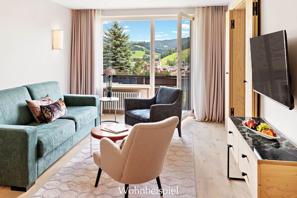Una sala de estar moderna con un sofá, un sillón y una mesa de comedor con fruta. Un ventanal ofrece vistas a un árbol y un pueblo lejano.
