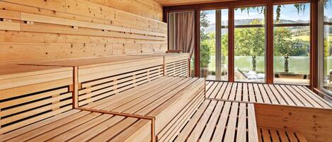 A wooden interior with benches and large windows offering a view of a lake and hills.