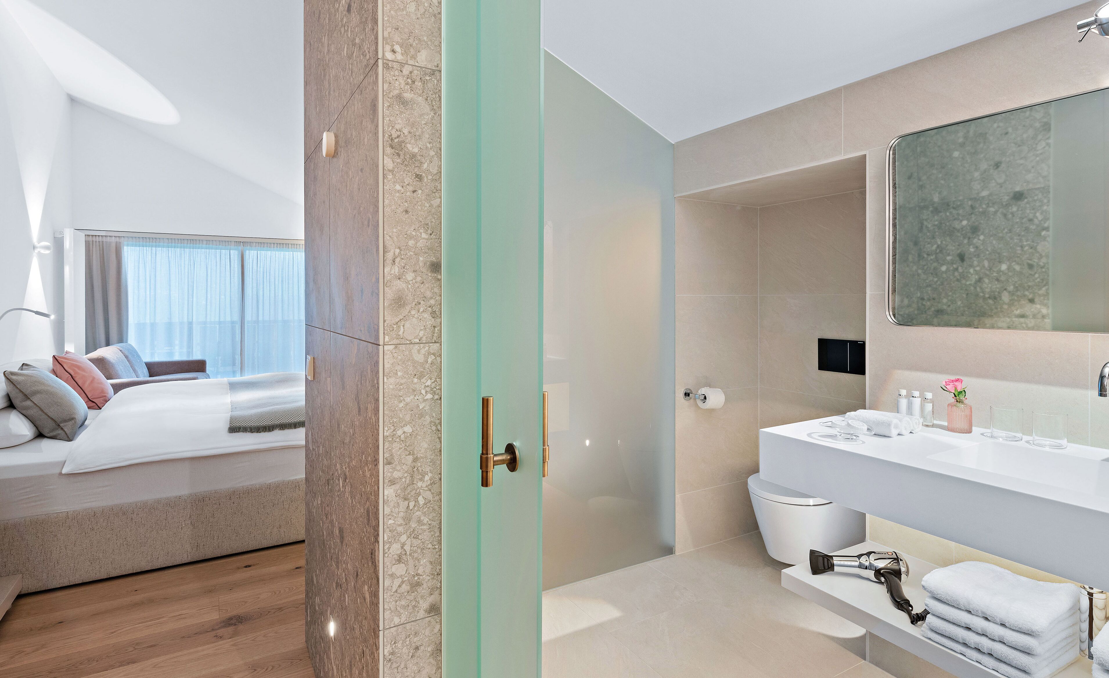 A modern hotel room with a bed, a bathroom with a large mirror, and a shower area.
