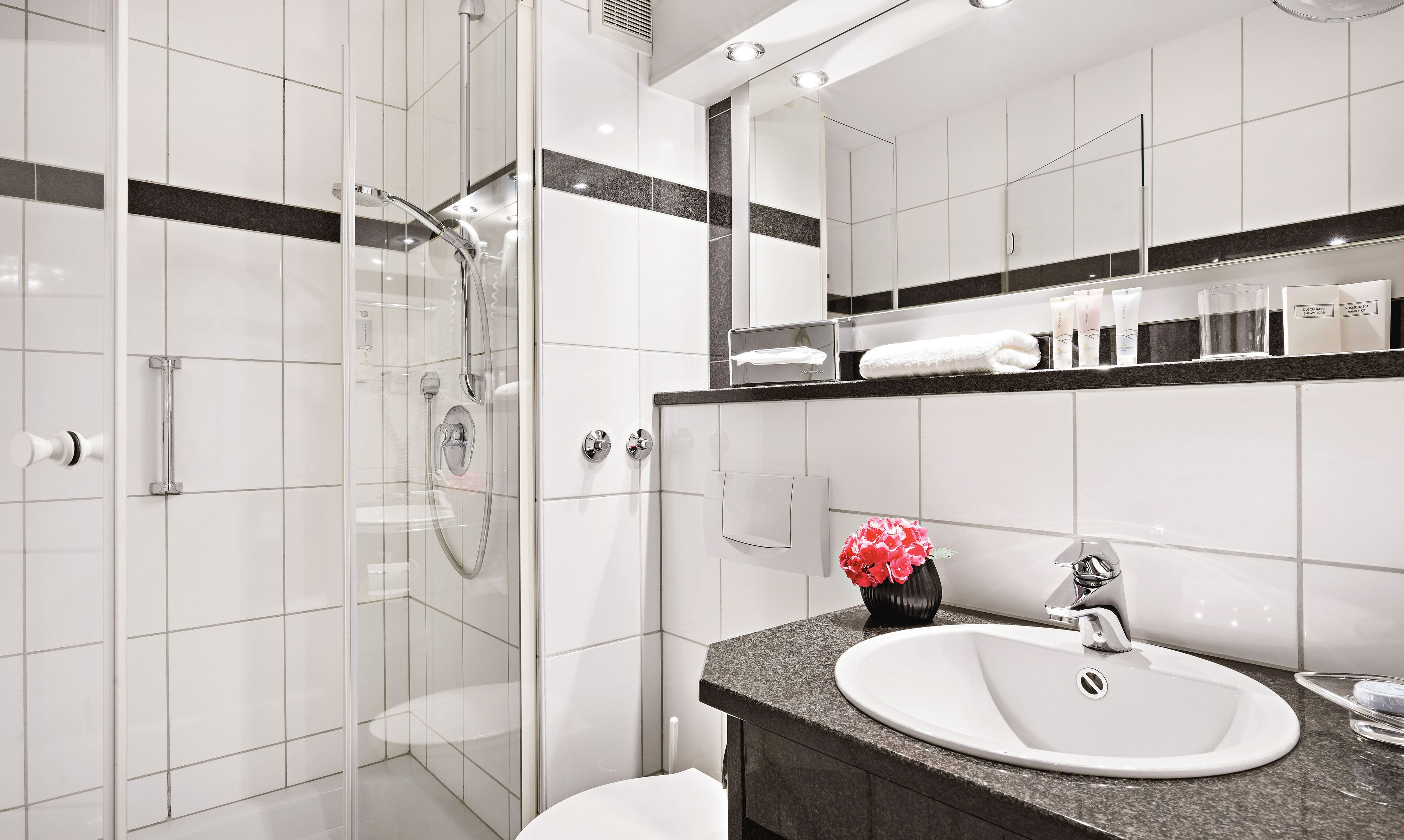 Un baño moderno con ducha de vidrio, un lavabo blanco y un mueble de tocador con artículos de aseo.