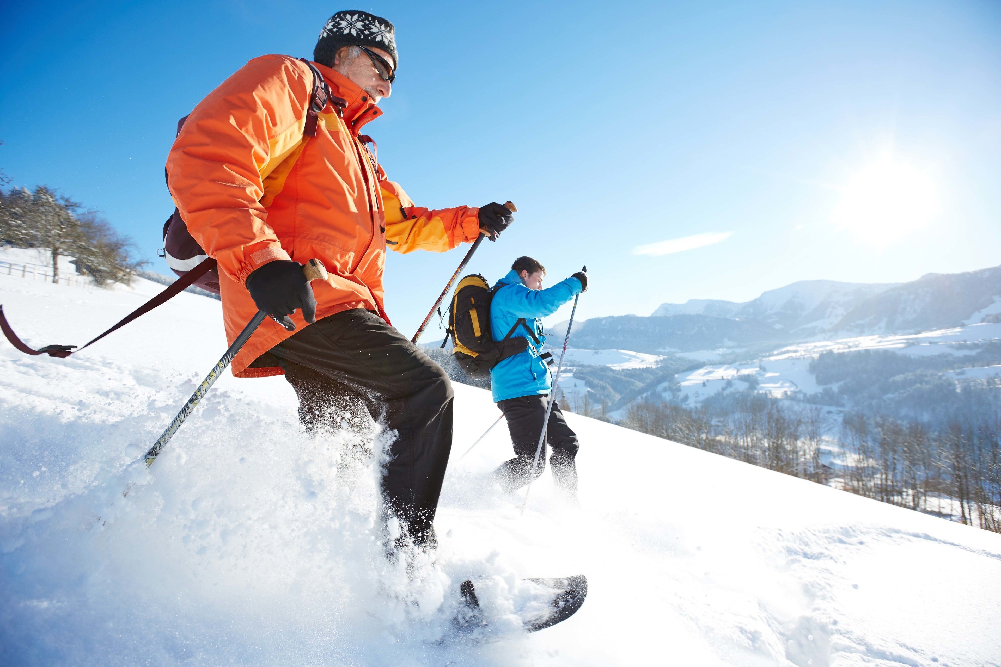 Two people skiing on a snowy slope with a clear sky and distant mountains.