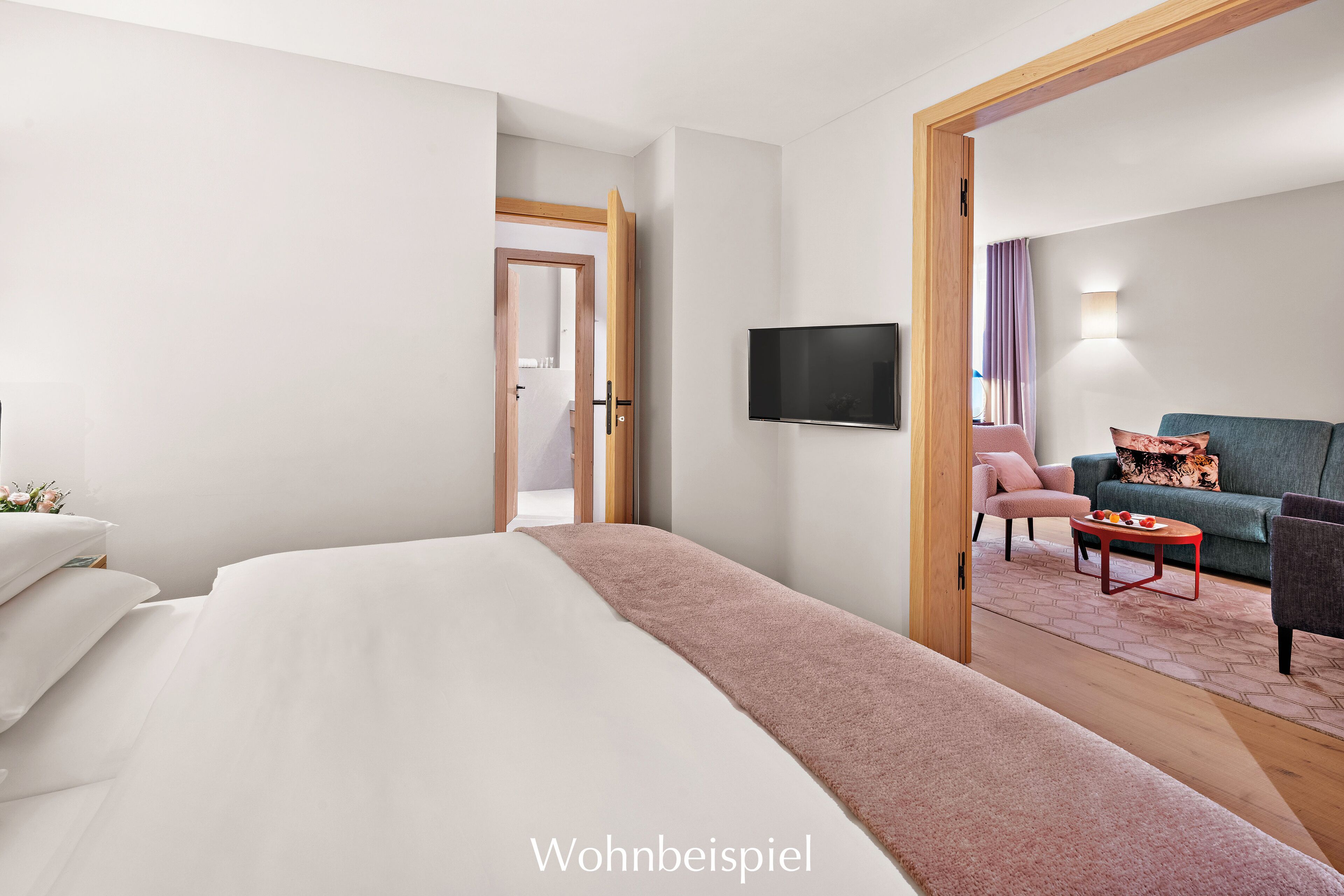 Ein modernes Hotelzimmer mit einem großen Bett, einem flachbildfernseher an der Wand, einer Sitzecke mit Sofa und Sesseln sowie einer Holztür, die in einen anderen Raum führt.
