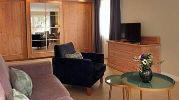 A living room with a sofa, armchair, wooden cabinet, TV, and a glass table with a vase.