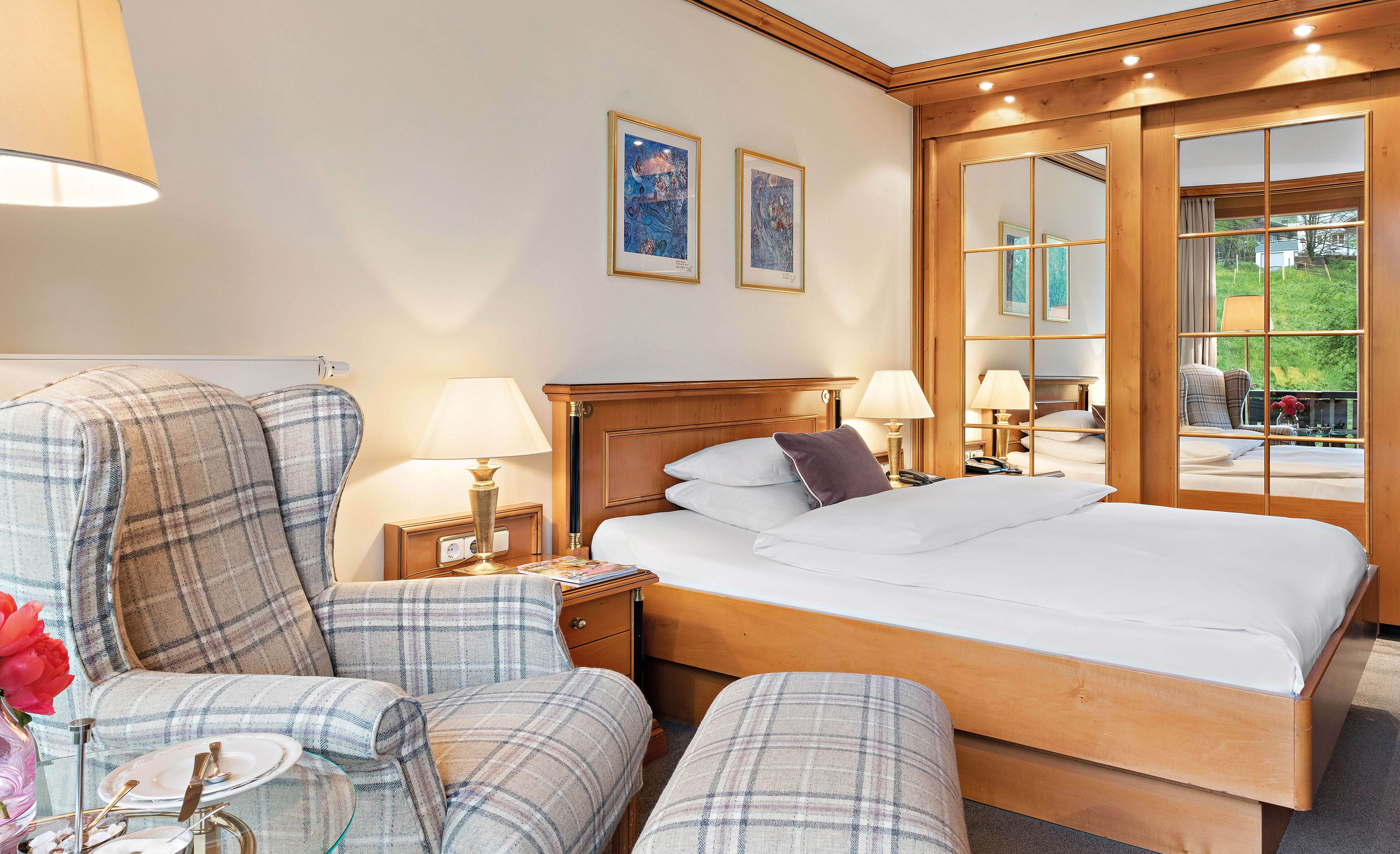 Une chambre d’hôtel avec un grand lit, deux tables de chevet avec des lampes, une chaise et une vue sur l’extérieur, visible à travers une porte vitrée.
