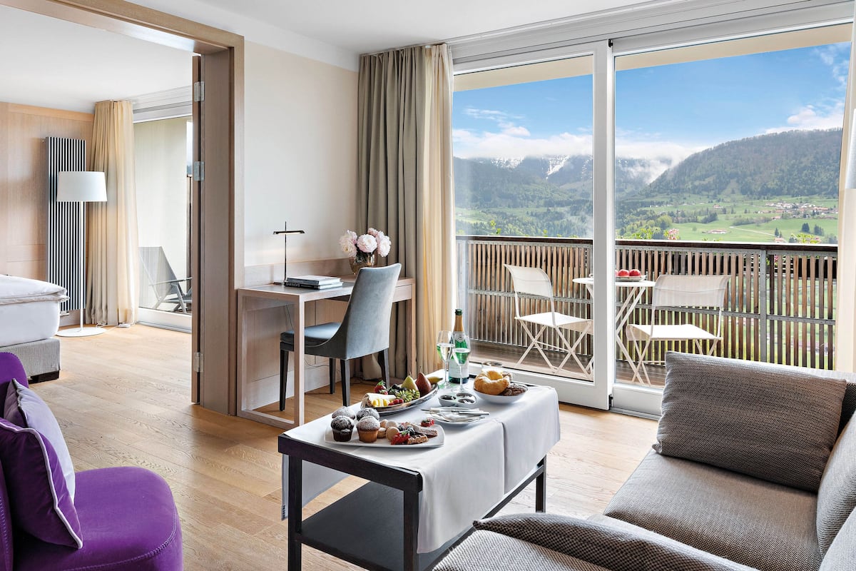 A modern hotel room with a balcony, a dining area, and a view of the mountains.