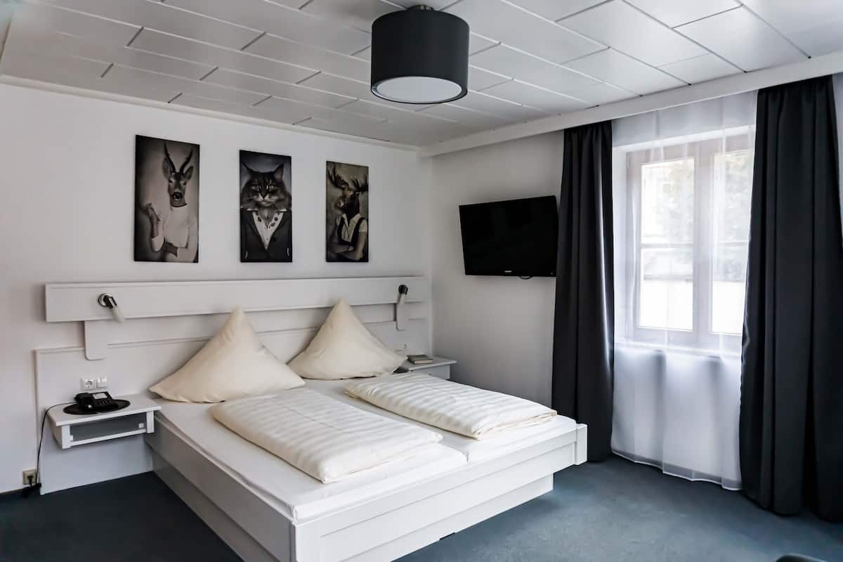 Habitación de hotel moderna con una cama blanca, un televisor de pantalla plana y obras de arte en la pared.