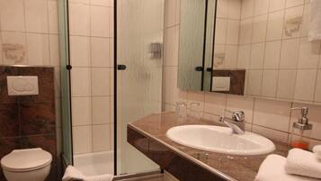 A bathroom with a glass shower enclosure, a white sink with a marble countertop, and a large mirror.
