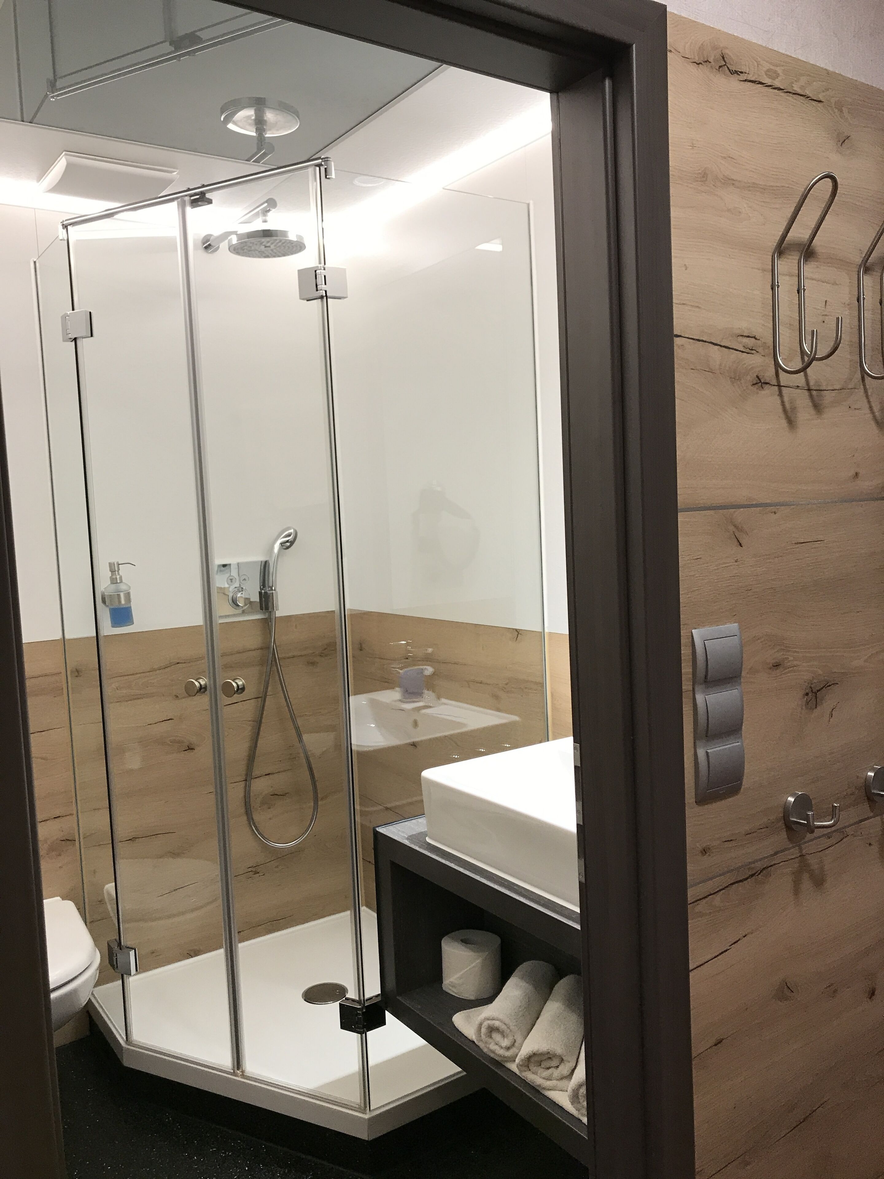 A modern bathroom with a glass-enclosed shower, a white sink, and a wooden vanity.