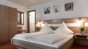Una cama doble con ropa de cama blanca, cabecera de madera, mesitas de noche con lámparas, un armario y una obra de arte colgada en la pared.