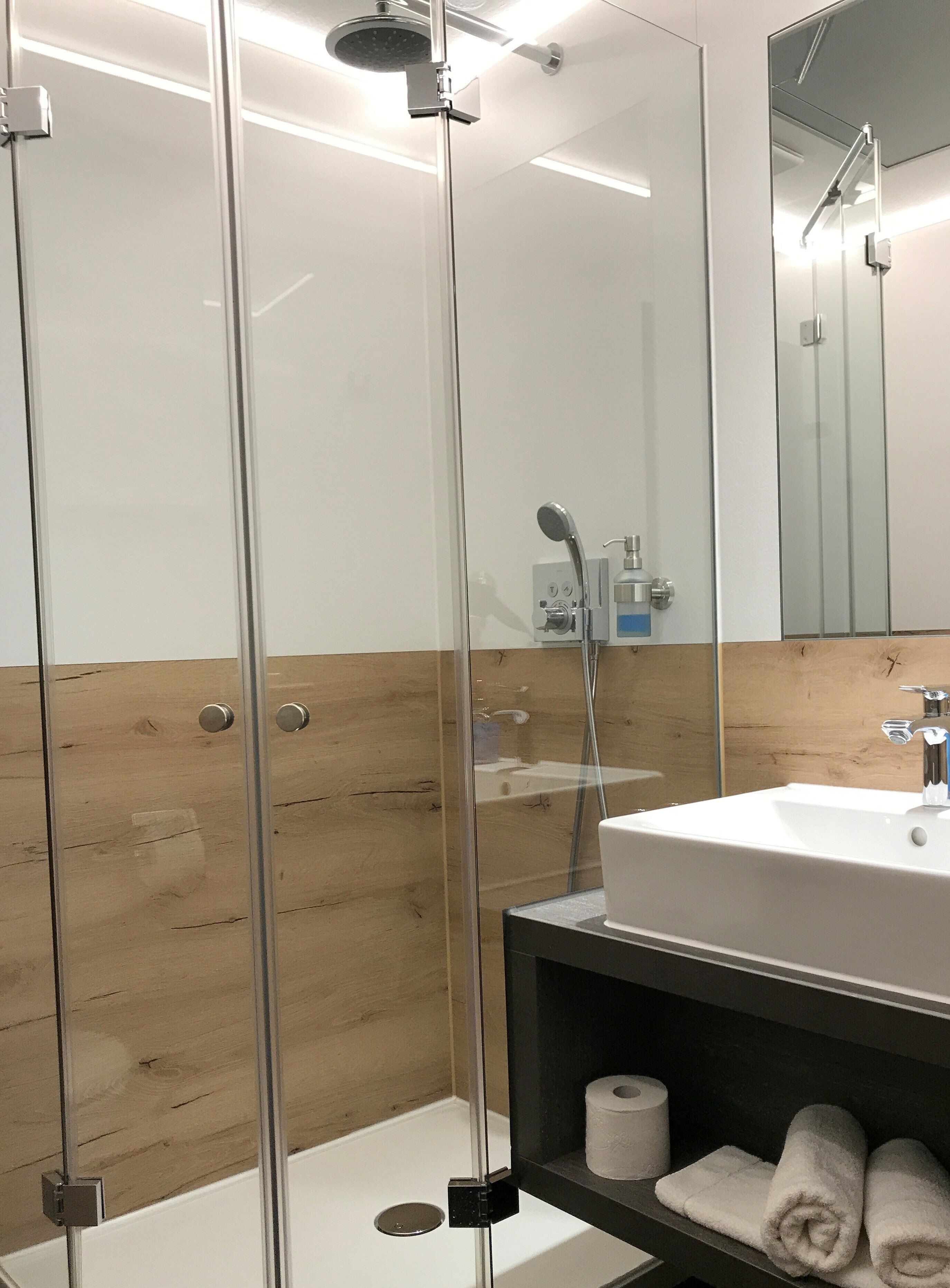 A modern bathroom with a glass-enclosed shower, a white sink, and wooden paneling.